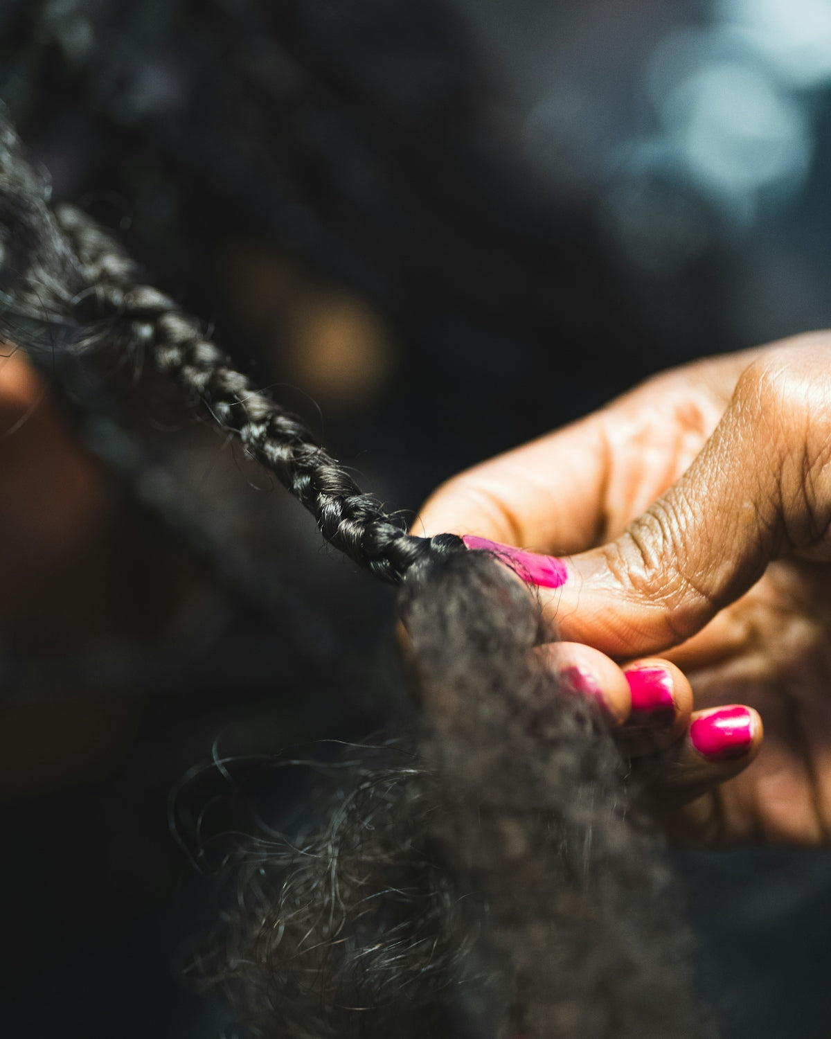 Close-up of hands braiding dark hair.